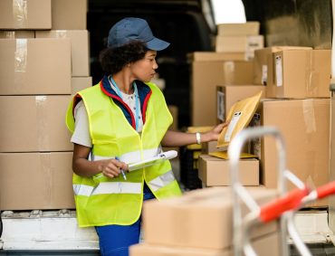 Female African American deliverer sorting packages in a van. Black female courier working and checking packages in a delivery van.